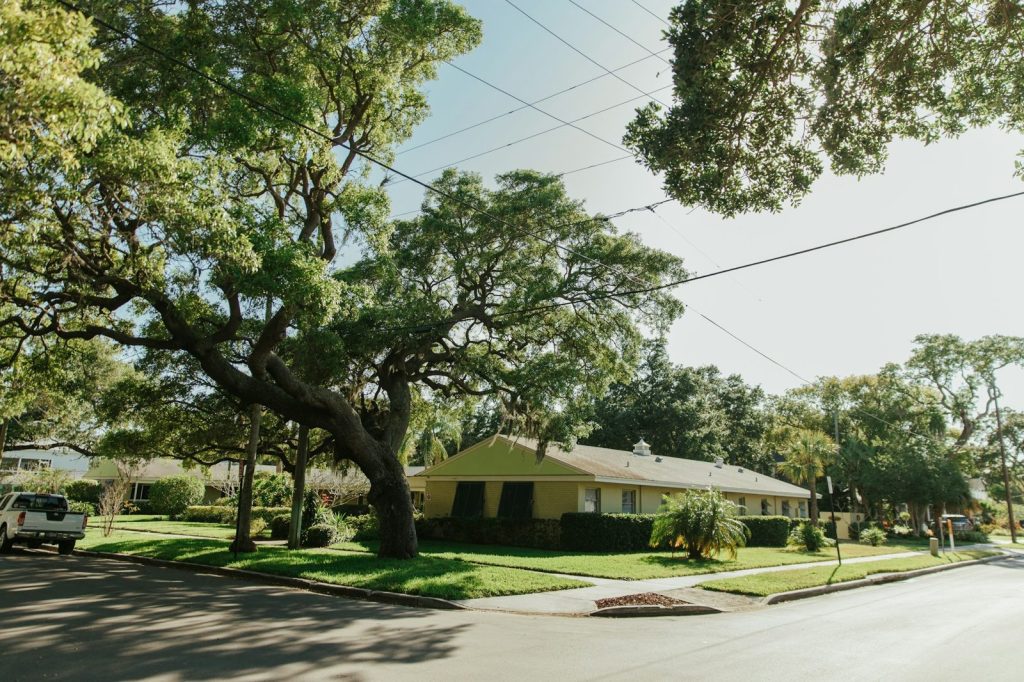 A single story home under large oak trees on a quiet Florida street